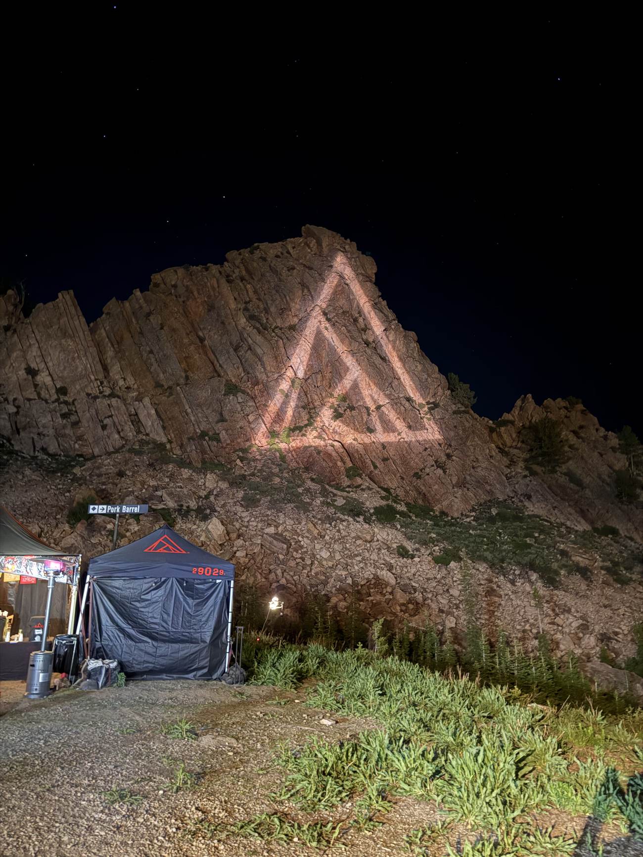 The 29029 triangle logo lit on the rock face at the summit under a starry night sky